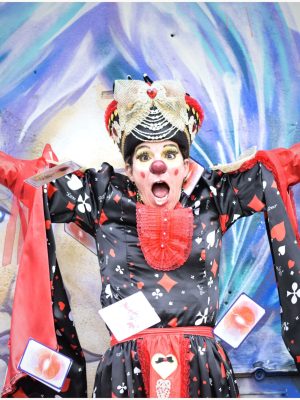 Artiste clown en costume rouge et noir lançant des cartes à jouer devant un fond mural coloré
